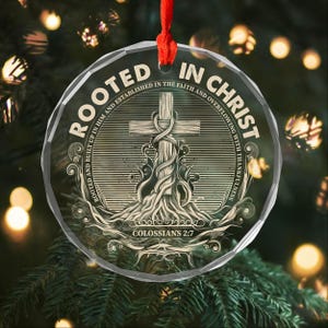 Peut inclure: Ornement de Noël rond et transparent avec l'inscription "ROOTED IN CHRIST" encerclant une croix. L'ornement est suspendu à un ruban rouge et porte le texte "COLOSSIANS 2:7".