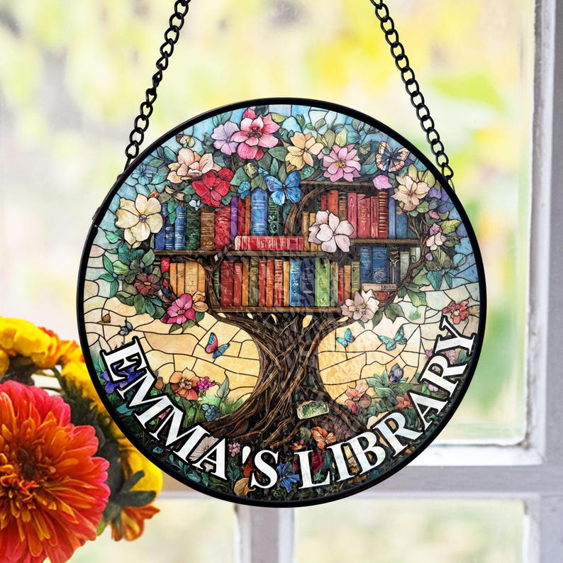 May include: A stained glass window hanging with a tree with books on its branches. The tree is surrounded by flowers and butterflies. The text "Emma's Library" is written on the bottom of the window.