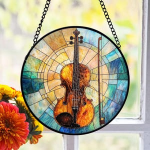 Op de afbeelding: Een hangend glas-in-loodraam met een kleurrijk, abstract ontwerp met een viool en strijkstok in het midden. De viool is bruin met een gele en oranje gradiënt. De achtergrond is een mix van blauw, groen en geel.