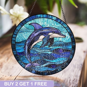 May include: A stained glass window hanging features a blue dolphin leaping out of the water. The dolphin is surrounded by blue and purple waves. The window is round and has a metal frame.