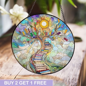 May include: A stained glass window hanging features a colorful tree with books as leaves and a staircase made of books leading up to a sun. The background is a blue and white sky.