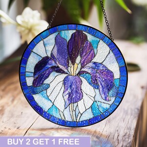 May include: A stained glass window hanging with a purple and blue iris flower design. The window is round and has a black metal frame.