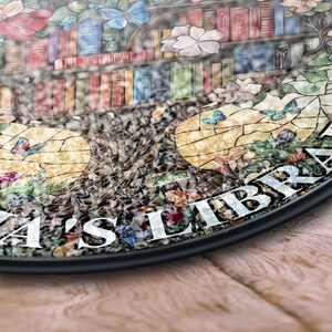 May include: A stained glass round sign with a tree design. The tree has books on the branches and butterflies flying around it. The sign says "Eliza's Library" in white lettering.