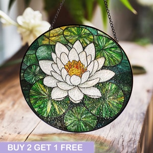 May include: A round stained glass window hanging from a chain. The window depicts a white water lily with a yellow center surrounded by green lily pads.