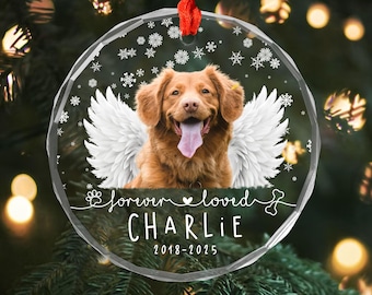 May include: A clear, round Christmas ornament with a photo of a dog with angel wings. The text "forever loved" and the dog's name, "CHARLIE", are printed on the ornament, along with the years 2018-2025. A red ribbon is attached for hanging.