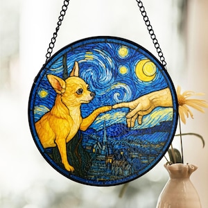 Op de afbeelding: Een hangend glas-in-loodraam toont een gele chihuahua die een hand in een sterrenhemel aanraakt. De hand reikt vanuit de rechterkant van de afbeelding. De achtergrond is een blauwe en gele sterrenhemel met een halve maan.