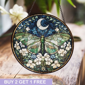May include: A stained glass window hanging with a crescent moon and a green butterfly with white flowers and blue flowers on a dark blue background.