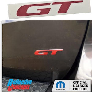 May include: Red "GT" emblem for a car. The emblem is made of reflective material and has a Mopar logo on the bottom. The emblem is an official licensed product.