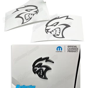 May include: Black and white decal of a snarling animal head with the text "Official Licensed Product" and the Mopar logo. The decal is on a white surface.