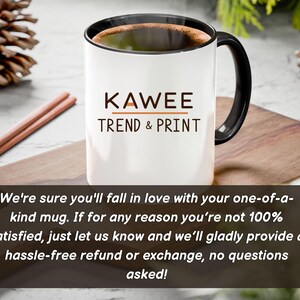 May include: White ceramic mug with a black handle and black rim. The mug has the text "KAWEE TREND & PRINT" printed on the front in brown and orange lettering. The mug is sitting on a wooden surface. The text below the mug reads: "We're sure you'll fall in love with your one-of-a-kind mug. If for any reason you're not 100% satisfied, just let us know and we'll gladly provide a hassle-free refund or exchange, no questions asked!"
