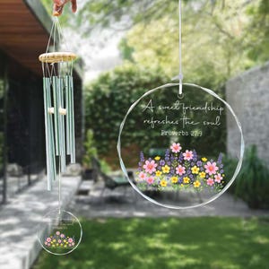 May include: A clear, round wind chime with a floral design and the text "A sweet friendship refreshes the soul Proverbs 27:9." The wind chime has silver-colored tubes and a wooden top. A smaller, matching charm hangs below.