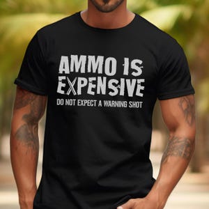 Peut inclure: T-shirt noir avec du texte blanc qui dit "Ammo is Expensive. Do not expect a warning shot."