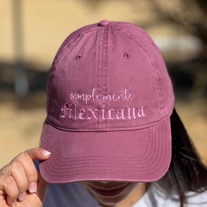May include: A burgundy baseball cap with the text "simplemente Mexicana" embroidered in pink.
