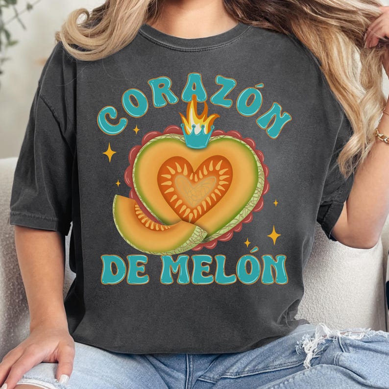 Op de afbeelding: Een donkergrijs T-shirt met een vintage-stijl grafische afbeelding van een hartvormige cantaloupe met een kroon en de tekst "CORAZ&Oacute;N DE MEL&Oacute;N".