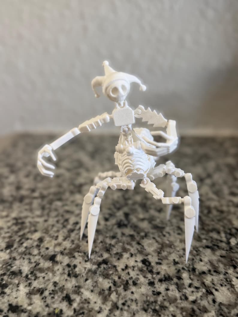Puede incluir: Una escultura blanca impresa en 3D de una figura esquel&eacute;tica parecida a un buf&oacute;n. Tiene un gorro de buf&oacute;n, un cuerpo segmentado y m&uacute;ltiples patas de ara&ntilde;a. La figura est&aacute; posando con un brazo extendido.