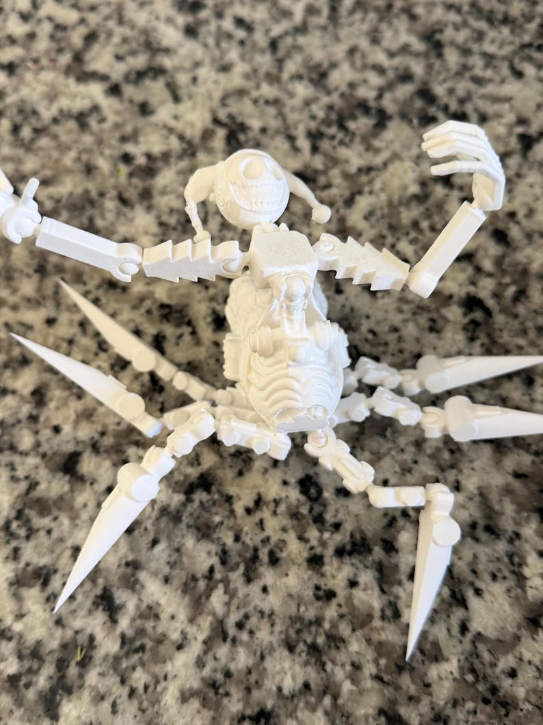Puede incluir: Una figura blanca articulada que se asemeja a una ara&ntilde;a, con una cara sonriente y extremidades articuladas. La figura tiene m&uacute;ltiples patas puntiagudas y brazos que se pueden posar. El dise&ntilde;o parece estar impreso en 3D, con l&iacute;neas de capa visibles.