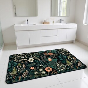 May include: A rectangular bathroom rug with a dark background and a floral pattern. The rug features various flowers in shades of white, peach, and green. The rug is placed on white tile flooring in front of a white double vanity.