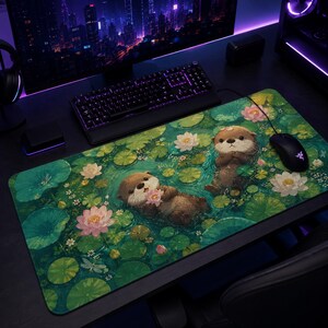 Puede incluir: Una alfombrilla de ratón rectangular grande con una ilustración caprichosa de dos nutrias flotando en un estanque lleno de nenúfares y flores de loto rosas y blancas. Las nutrias son marrones con pelaje marrón claro.