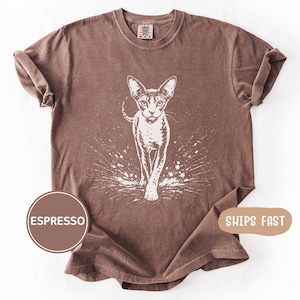 May include: Espresso-colored t-shirt featuring a white graphic of a cat walking forward with a splash effect. The shirt has a crew neck and short sleeves. The word "ESPRESSO" is in a brown circle on the bottom left.