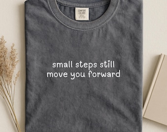 Camiseta "Pequeños pasos te hacen avanzar" con colores cómodos y cita positiva.