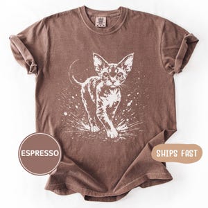 May include: Espresso-colored t-shirt featuring a white graphic of a cat walking forward with a splash effect. The shirt has rolled-up sleeves and a crew neck. The text "ESPRESSO" is in a brown circle.