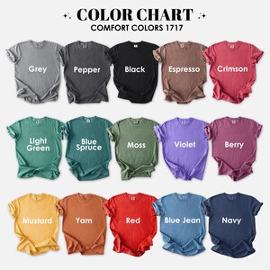 May include: A color chart displaying various Comfort Colors 1717 t-shirts. The shirts are arranged in rows, showcasing a range of colors including grey, black, red, and blue. Each shirt is labeled with its respective color name, such as "Grey," "Black," and "Red."