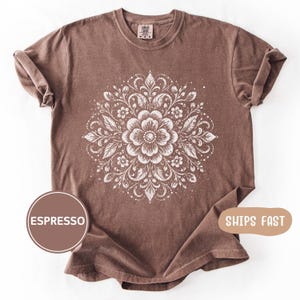 May include: Espresso-colored t-shirt featuring a white floral mandala design. The round neck tee has rolled-up sleeves and a Comfort Colors tag. The shirt has the word "ESPRESSO" printed on a brown circle.