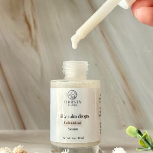 May include: A close-up of a white serum bottle with a dropper dispensing liquid. The bottle is labeled "Milky Calm Drops" and "Colloidal Oat Serum" by Thirsty Kamel. The bottle contains 1 fl oz (30 ml) of serum. The background is a marble-like surface.