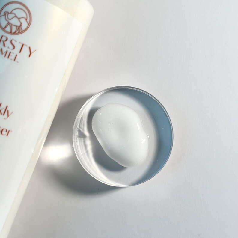 Pu&ograve; includere: Un piccolo ciuffo di crema viso bianca in una ciotola di vetro trasparente. La crema &egrave; liscia e densa, e la ciotola &egrave; rotonda e poco profonda.