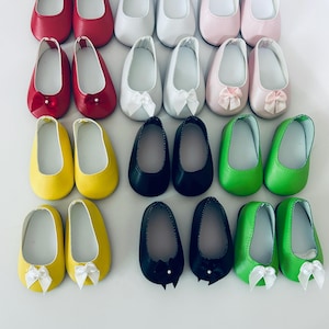 May include: A collection of doll shoes in various colors, including red, white, pink, yellow, black, and green. Some shoes have bows. The shoes are arranged in rows on a white surface.