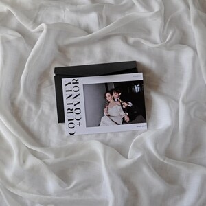 May include: A white card with black text that reads "COURTNEY + CONNOR" and a photo of a couple in a formal setting. The card is on a white fabric background.