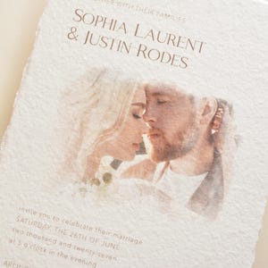 May include: A wedding invitation with the names SOPHIA LAURENT & JUSTIN RODES printed in brown. The invitation features a watercolor image of a couple and the date of the wedding. The invitation is on textured paper.