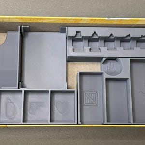 May include: A gray plastic organizer insert for a board game box. The insert has compartments for cards, dice, and other game pieces. The insert is designed to fit a specific board game box.