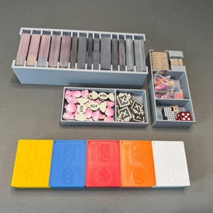 May include: A set of six storage boxes for organizing game pieces. The boxes are made of sturdy cardboard and have a variety of colors, including yellow, blue, red, orange, and white. The boxes are labeled with different symbols and designs.