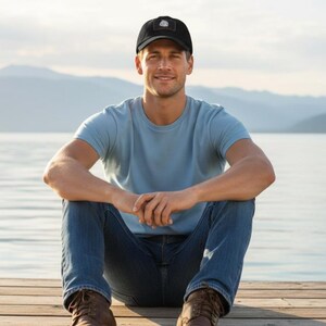 May include: A black baseball cap with a small rectangular patch on the front, a light blue crew neck t-shirt, and dark blue denim jeans. The cap features a centred white graphic design on the patch, paired with casual clothing for a simple look.