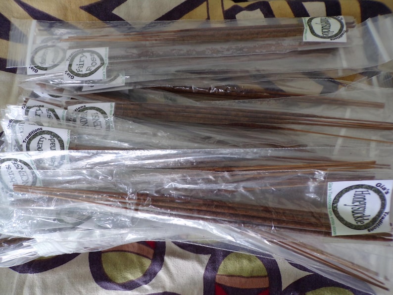 May include: A close-up of a stack of individually wrapped incense sticks. The sticks are brown and have a variety of scents, including "Honeysuckle", "Cherry Blossom", and "Fairy Frost".