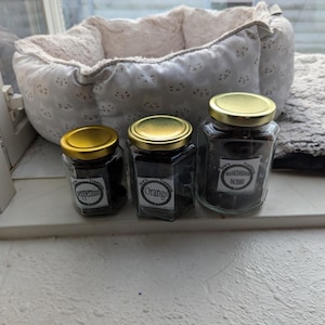 Peut inclure: Trois bocaux en verre avec des couvercles dorés remplis de bonbons noirs. Les bocaux sont étiquetés "Peppermint", "Orange" et "Frankincense & Myrrh".