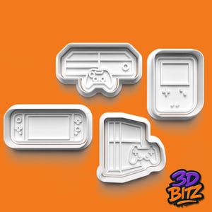 May include: Four white plastic cookie cutters shaped like retro video game consoles and controllers. The shapes include a handheld console, a console with a controller, and a game console with a controller. The background is orange.