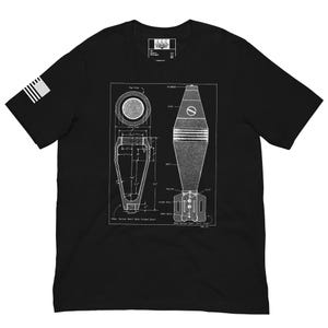 May include: Black t-shirt featuring a white blueprint design of a mortar shell. The design includes detailed diagrams and labels. An American flag is on the left sleeve. The shirt has a crew neck and short sleeves.