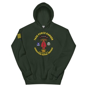 May include: Dark green hooded sweatshirt with the text "TASK FORCE RANGER" and various military patches. The design includes the words "OPERATION GOTHIC SERPENT MOGADISHU 1993" in yellow. A yellow stripe is on the left sleeve.