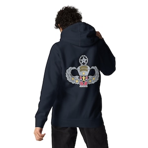 May include: A navy blue hooded sweatshirt featuring a graphic on the back. The design displays a silver parachute emblem with wings, a star, and the text RANGER AIRBORNE. Below the parachute is a red and black shield with a yellow figure.