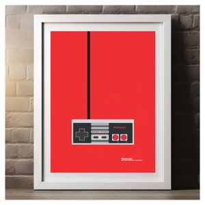May include: Framed print featuring a minimalist design of a classic Nintendo controller against a vibrant red background. The controller is gray and black with red buttons. The Nintendo logo is visible. A black cable extends from the controller.