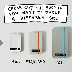 May include: Image of three rectangular, light gray objects labeled "MINI", "STANDARD", and "XL". Each has a colored stripe: white, orange, and blue. Text above reads "CHECK OUT THE SHOP IF YOU WANT TO ORDER A DIFFERENT SIZE". A quarter is next to the objects.