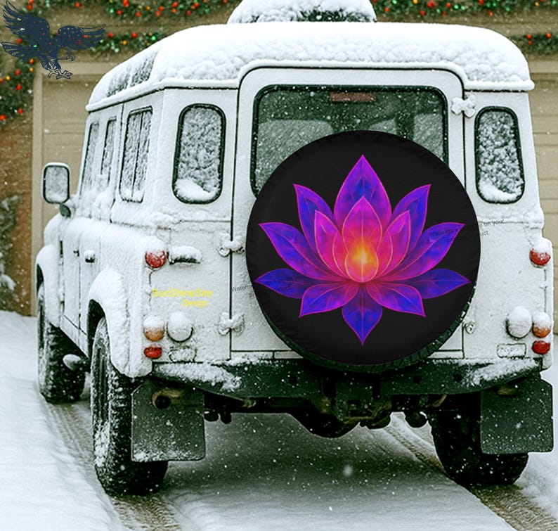 May include: A white SUV covered in snow with a spare tire cover featuring a vibrant lotus flower design in shades of purple, pink, and yellow against a black background. The vehicle is parked in a snowy environment.