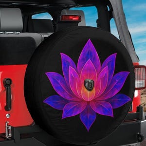May include: Black spare tire cover featuring a vibrant lotus flower design in shades of purple, pink, and yellow. The cover is mounted on a red Jeep, with a glimpse of the interior and a scenic background.