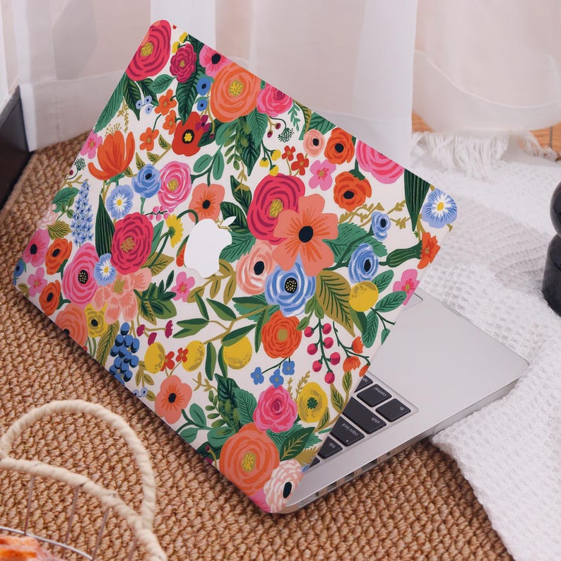 May include: A laptop computer with a floral patterned case. The case features a white background with a colorful array of flowers in shades of pink, orange, blue, and yellow. The Apple logo is visible on the case.