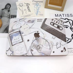 May include: A white laptop skin with a retro-inspired design featuring a cassette tape, a mini disc, a portable music player, and a cartoon bear. The design is in shades of gray and white with a few black accents. The text "HEISEI MUSIC" and "ALBUM" are visible on the skin.