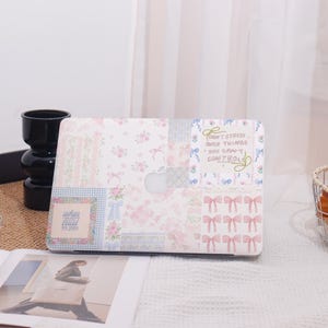 May include: A white laptop case with a patchwork design featuring floral patterns, bows, and the text "Don't stress over things you can't control." The case has a cutout for the Apple logo.