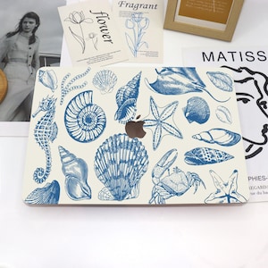 Könnte beinhalten: Eine weiße Laptop-Haut mit einem blauen und weißen Muschel-Design. Das Design zeigt eine Vielzahl von Muscheln, Seesternen, einem Krebs und einem Seepferdchen.