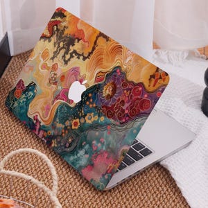 Op de afbeelding: Een laptop met een kleurrijk, abstract ontwerp. De hoes heeft een levendige mix van oranje, geel, blauwgroen en roze tinten, met bloem- en wolkenachtige patronen. Het Apple-logo is zichtbaar op het deksel van de laptop.